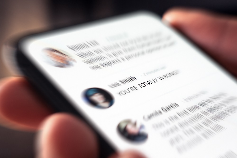 יד אוחזת בסמארטפון המציג תגובות מתלהמות ברשת חברתית